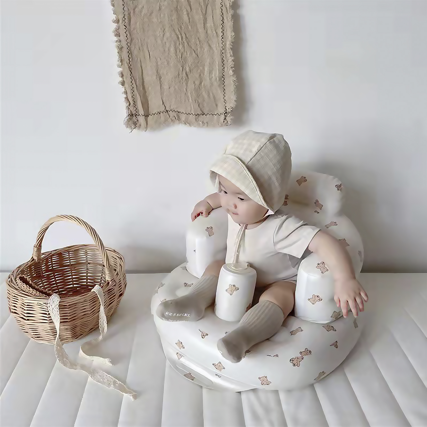Un bebé con gorro sentado en una silla inflable con tema de osos, con una canasta.
