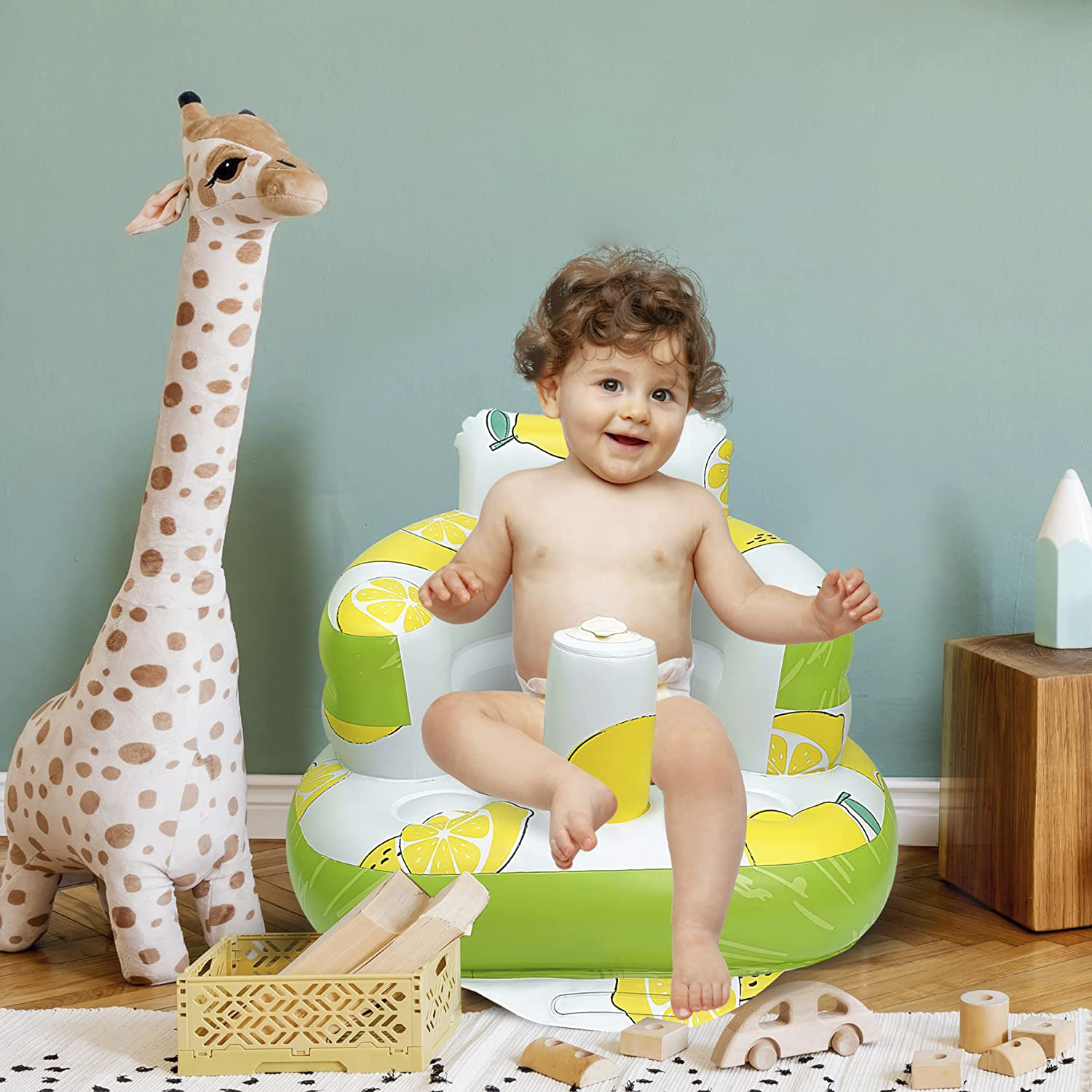 Un bebé sentado en una silla inflable de limones, sonriendo. Juguetes de jirafa y madera cerca.