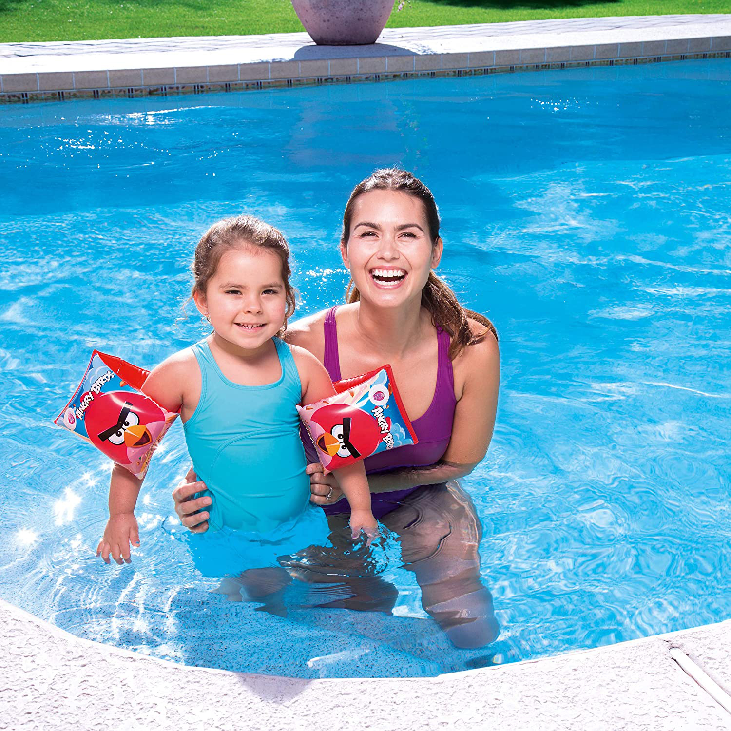 Una niña en una piscina sosteniendo una pelota de playa amarilla con estrellas, sonriendo.