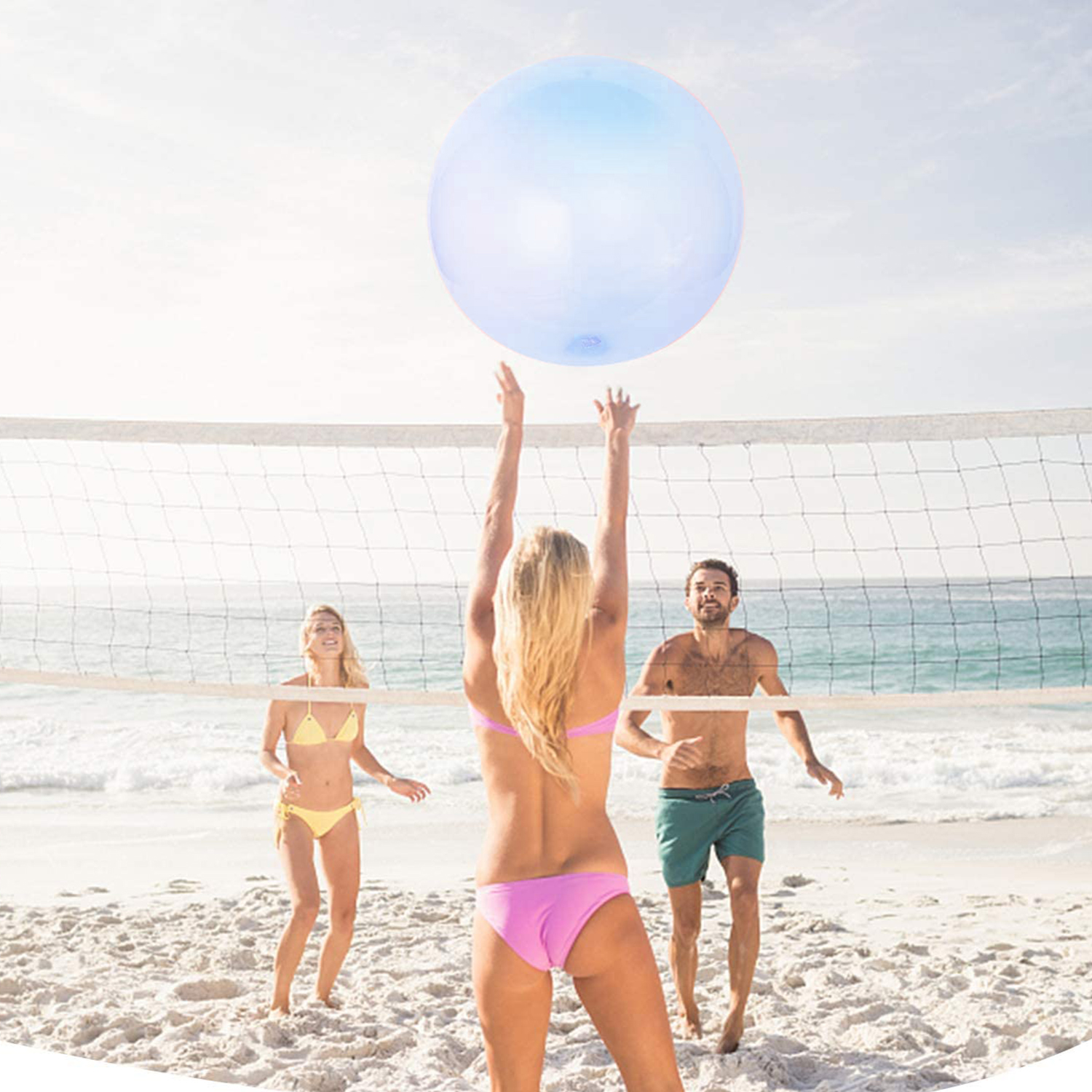 Tres personas jugando voleibol con una gran bola de burbujas azul y transparente en la playa.