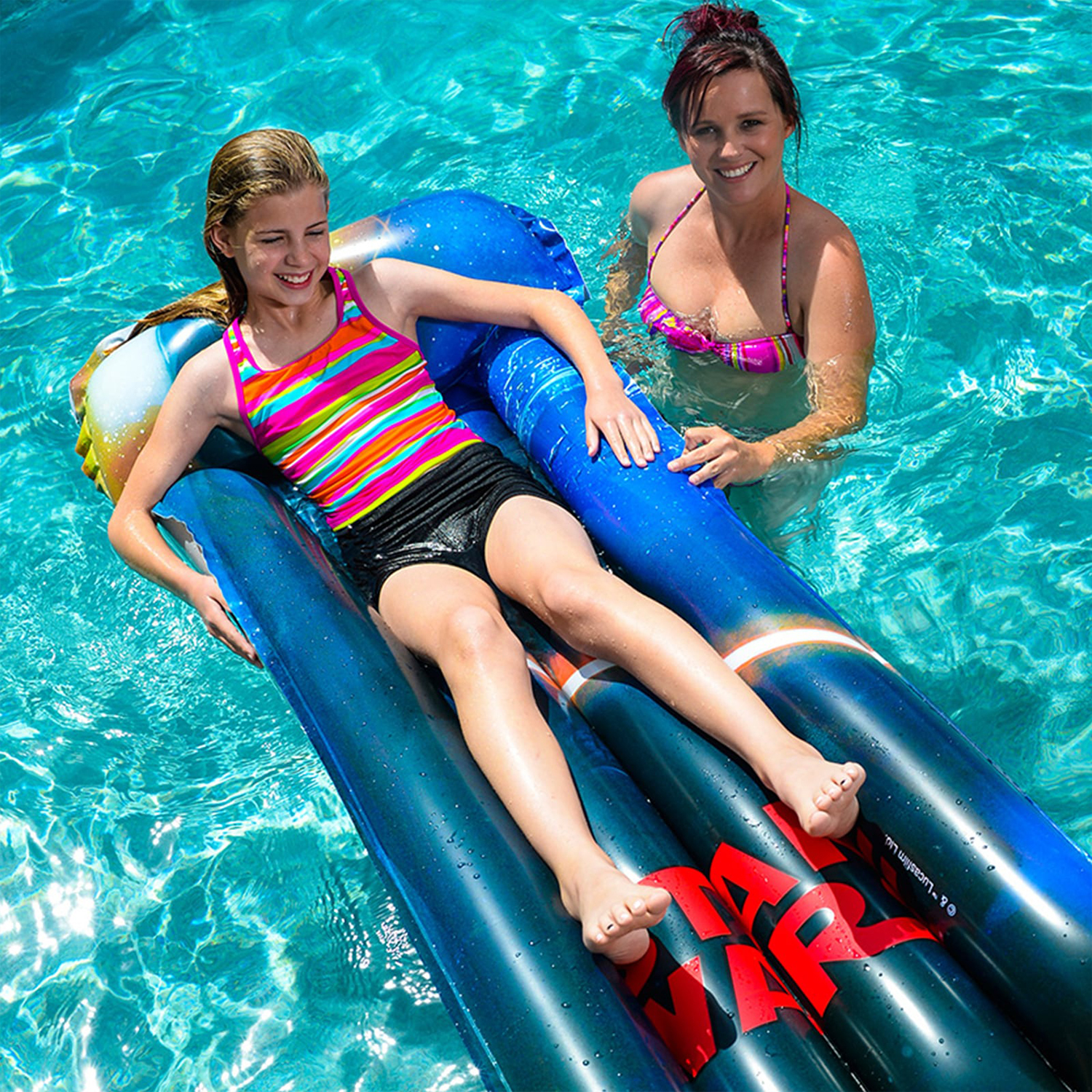 Due donne in piscina, una su un canotto blu, l'altra in acqua, sorridenti.