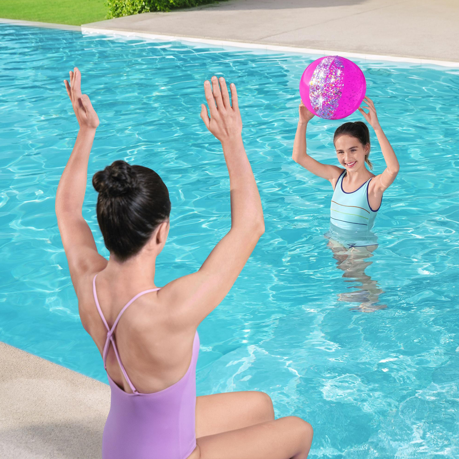 Una madre e sua figlia giocano in piscina, la figlia tiene in mano una palla rosa glitterata.