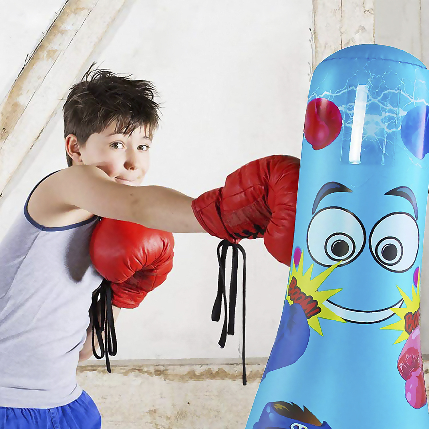 Un niño con camiseta sin mangas y pantalones cortos golpea un saco de boxeo inflable azul.