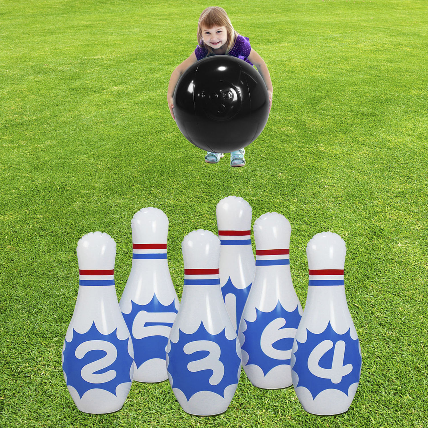 Una niña sosteniendo una gran bola de bolos negra sobre seis bolos inflables sobre hierba verde.
