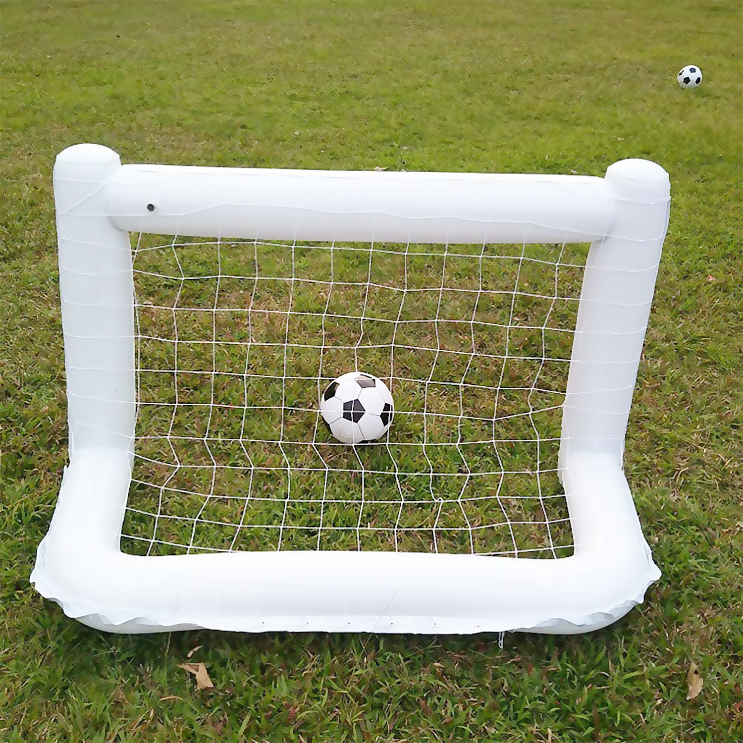 Una portería de fútbol inflable blanca con un balón de fútbol dentro, en un césped verde.