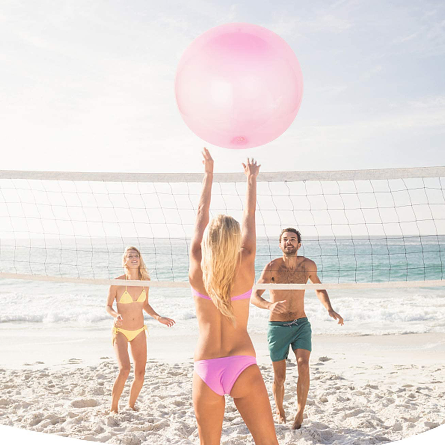 Tres personas jugando voleibol en la playa. Una mujer golpea una pelota rosa.