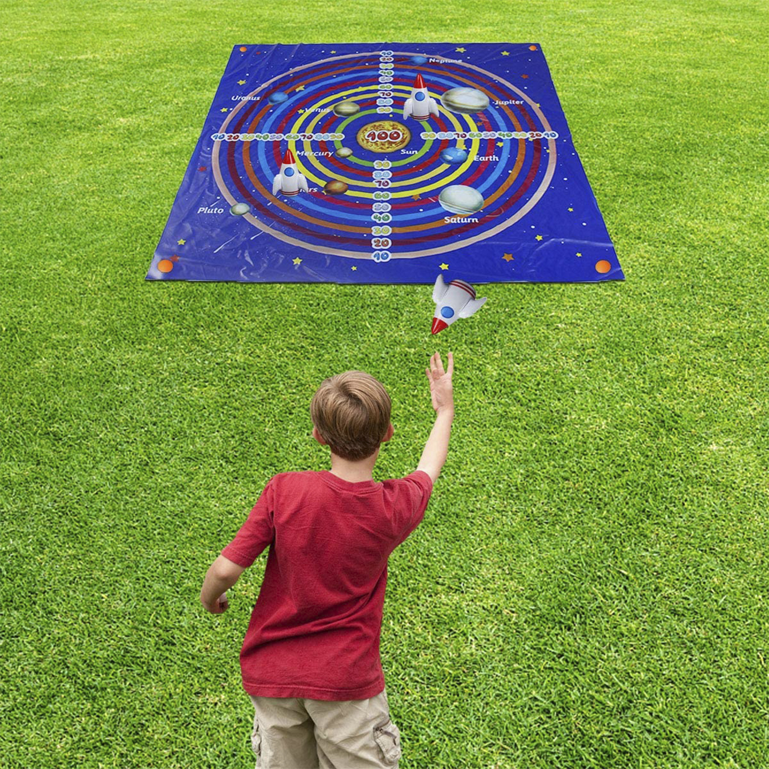 Un niño lanzando un cohete hacia un tapete de juego del sistema solar sobre césped verde al aire libre.