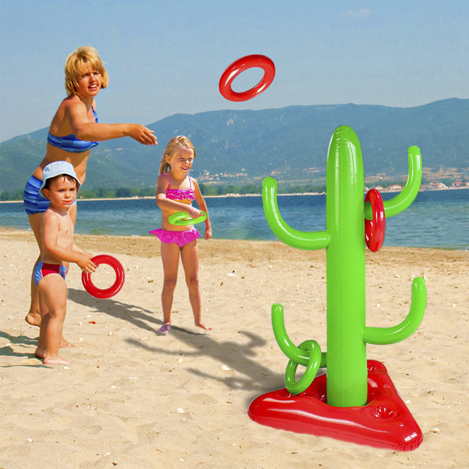 Familia jugando al lanzamiento de aros en la playa con cactus inflable, cielo azul y mar de fondo.
