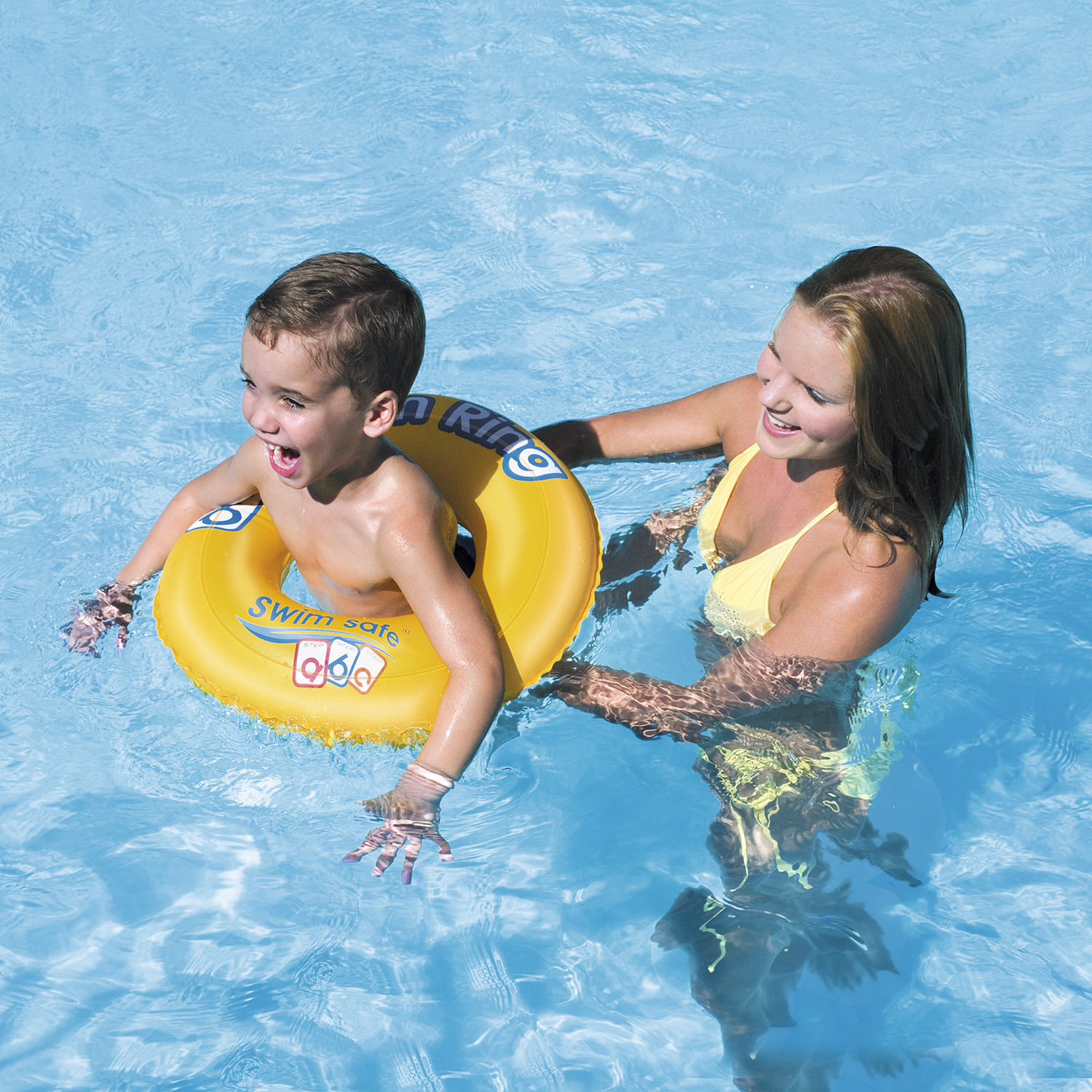 Un niño en un flotador con una mujer en bikini amarillo en una piscina, ambos sonriendo. El flotador es amarillo.
