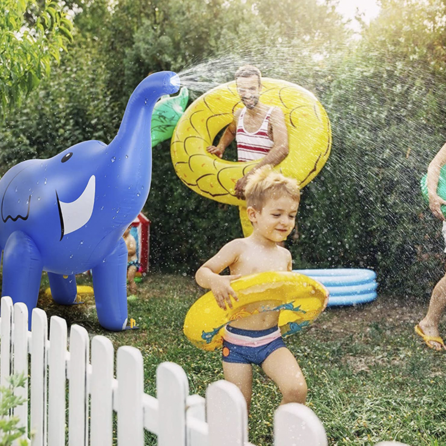 Un'irrigatore a forma di elefante blu con acqua spruzzata, un ragazzo e un uomo in giardino.