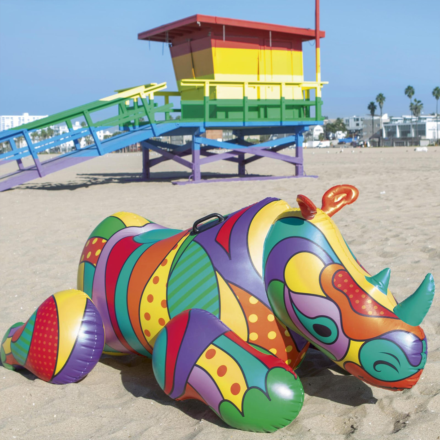 Un rinoceronte gonfiabile colorato su una spiaggia sabbiosa, con una torretta di salvataggio sullo sfondo.