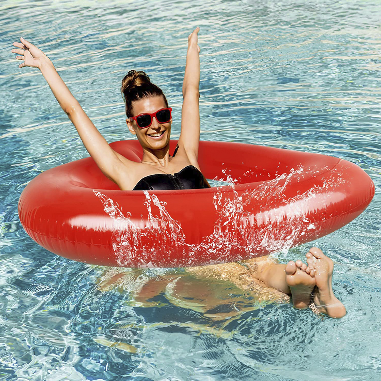 Una mujer en un flotador de tubo rojo en una piscina, con los brazos en alto y sonriendo.