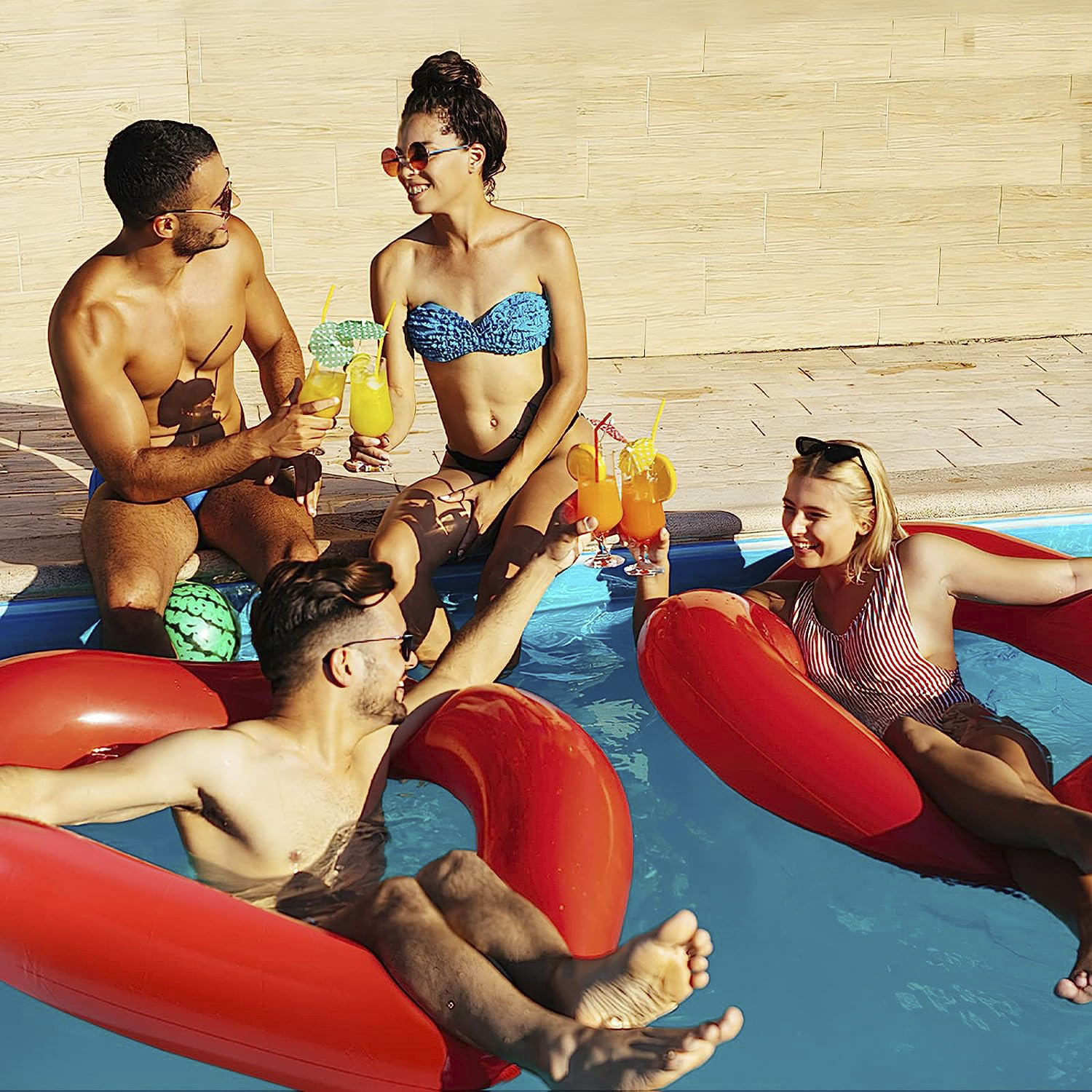 Grupo de amigos en una piscina, disfrutando de bebidas y relajándose en balsas inflables rojas.