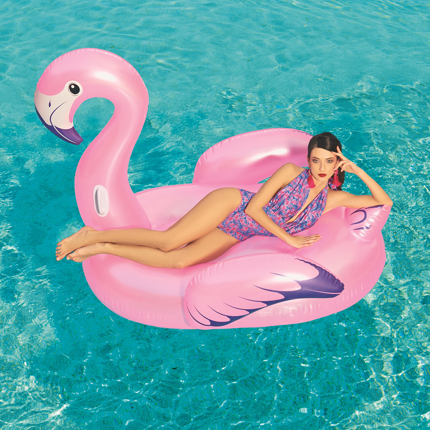 Una donna su un galleggiante a forma di fenicottero rosa, in costume da bagno, sdraiata su un fianco in piscina.
