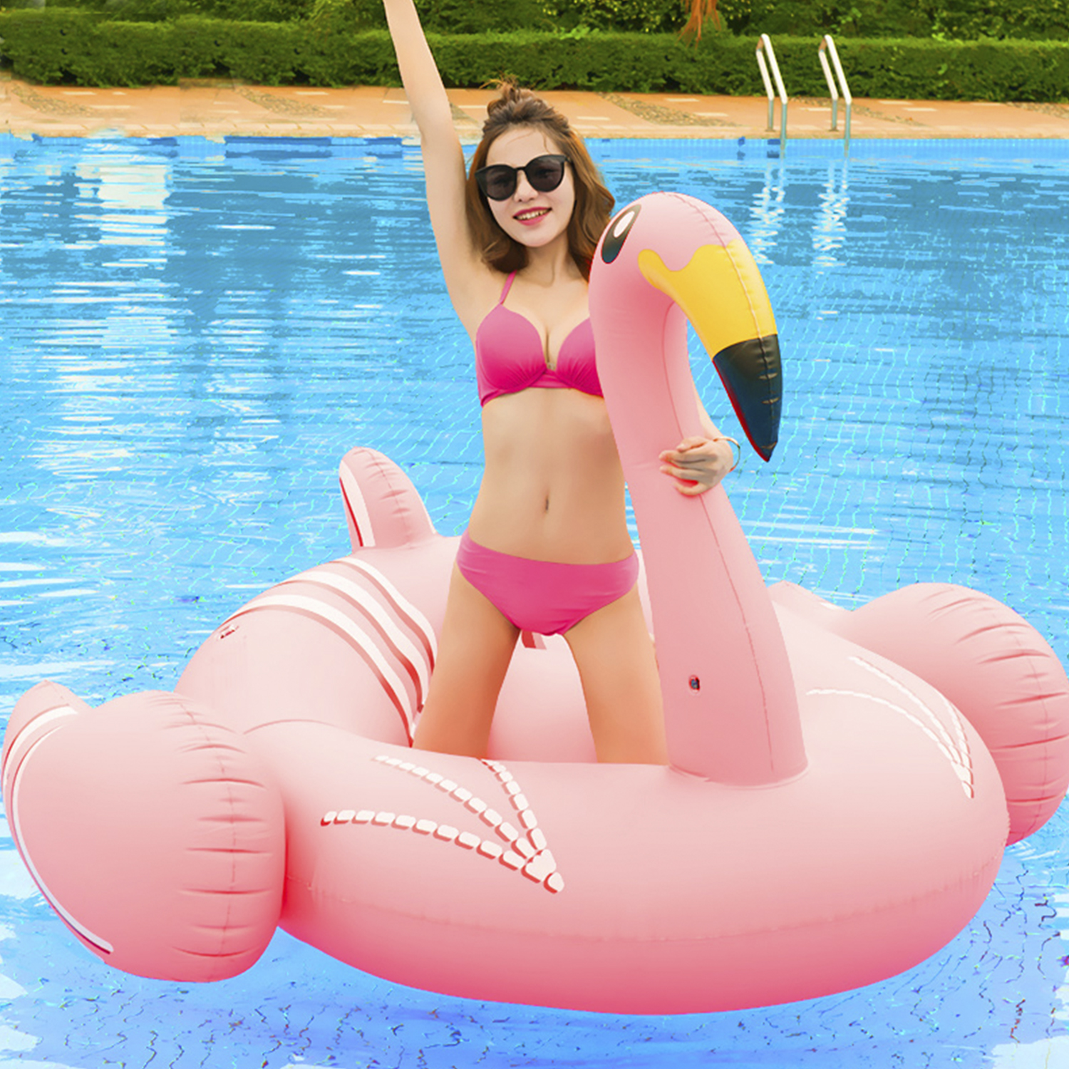 Donna su un galleggiante a forma di fenicottero rosa in una piscina. Indossa un bikini rosa e occhiali da sole.