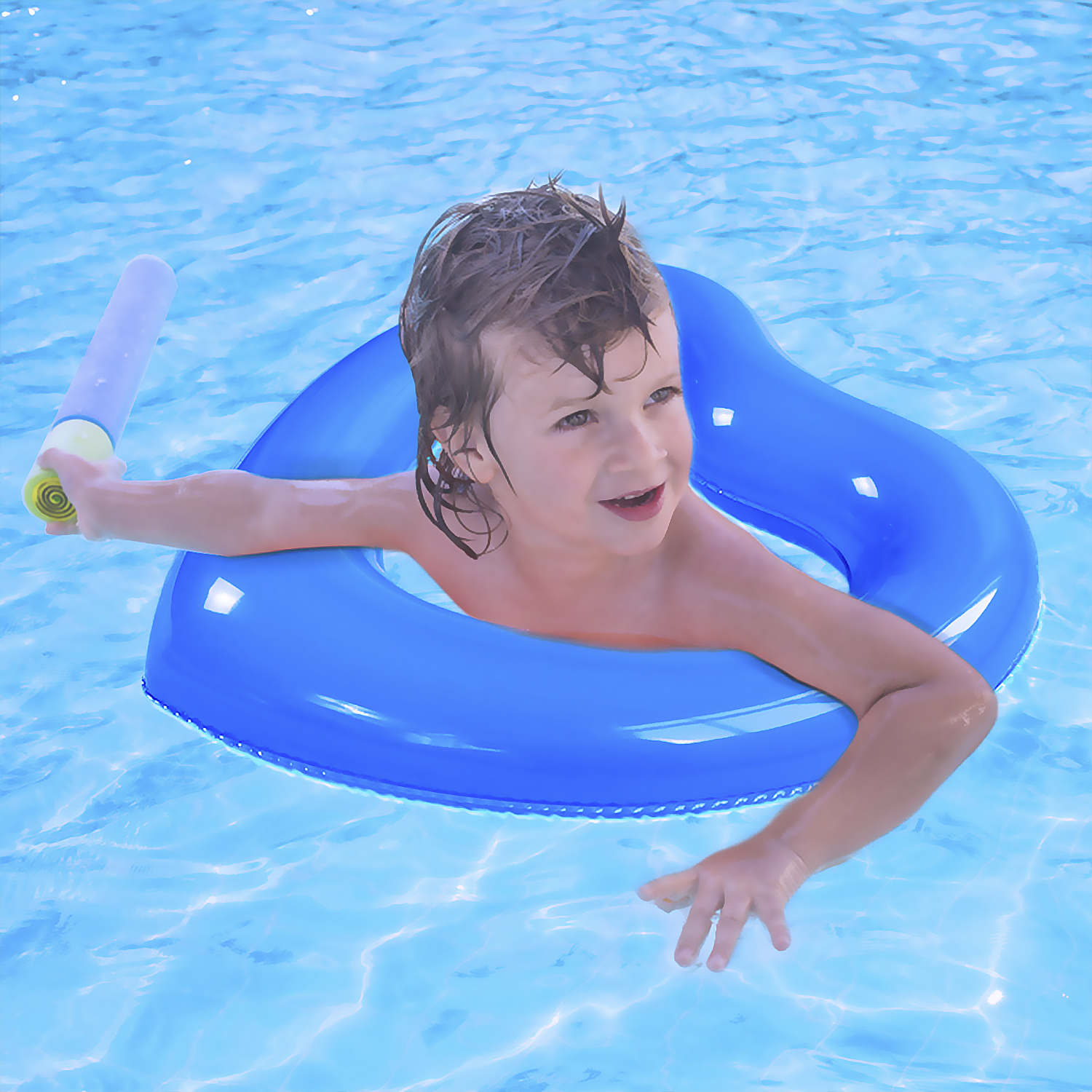 Un niño pequeño en un flotador azul en una piscina, sosteniendo una pistola de agua.
