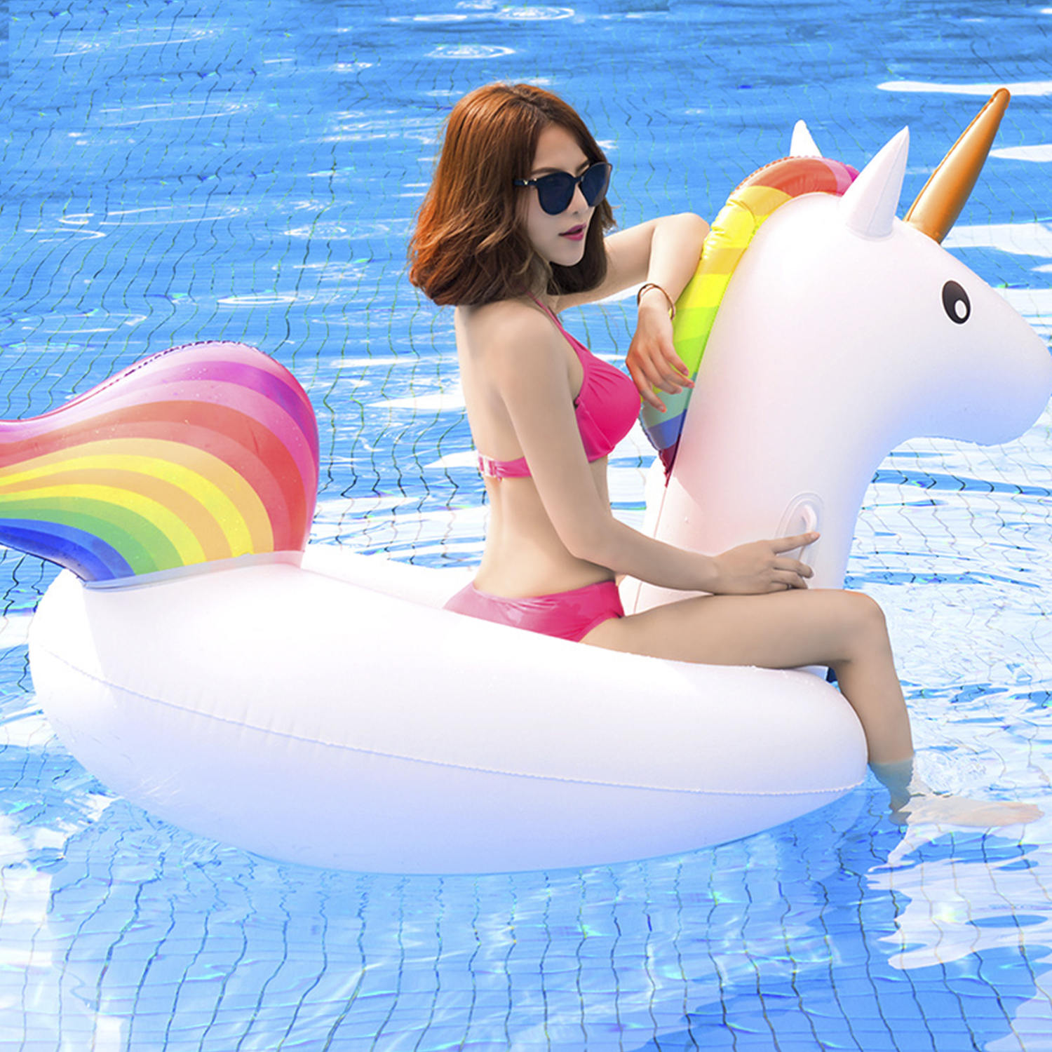Donna in bikini rosa seduta su un galleggiante unicorno bianco in una piscina blu. Criniera e coda arcobaleno.