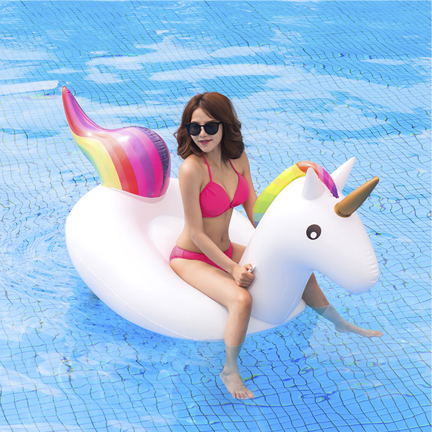 Una donna su un galleggiante unicorno bianco in piscina con occhiali da sole e bikini rosa.