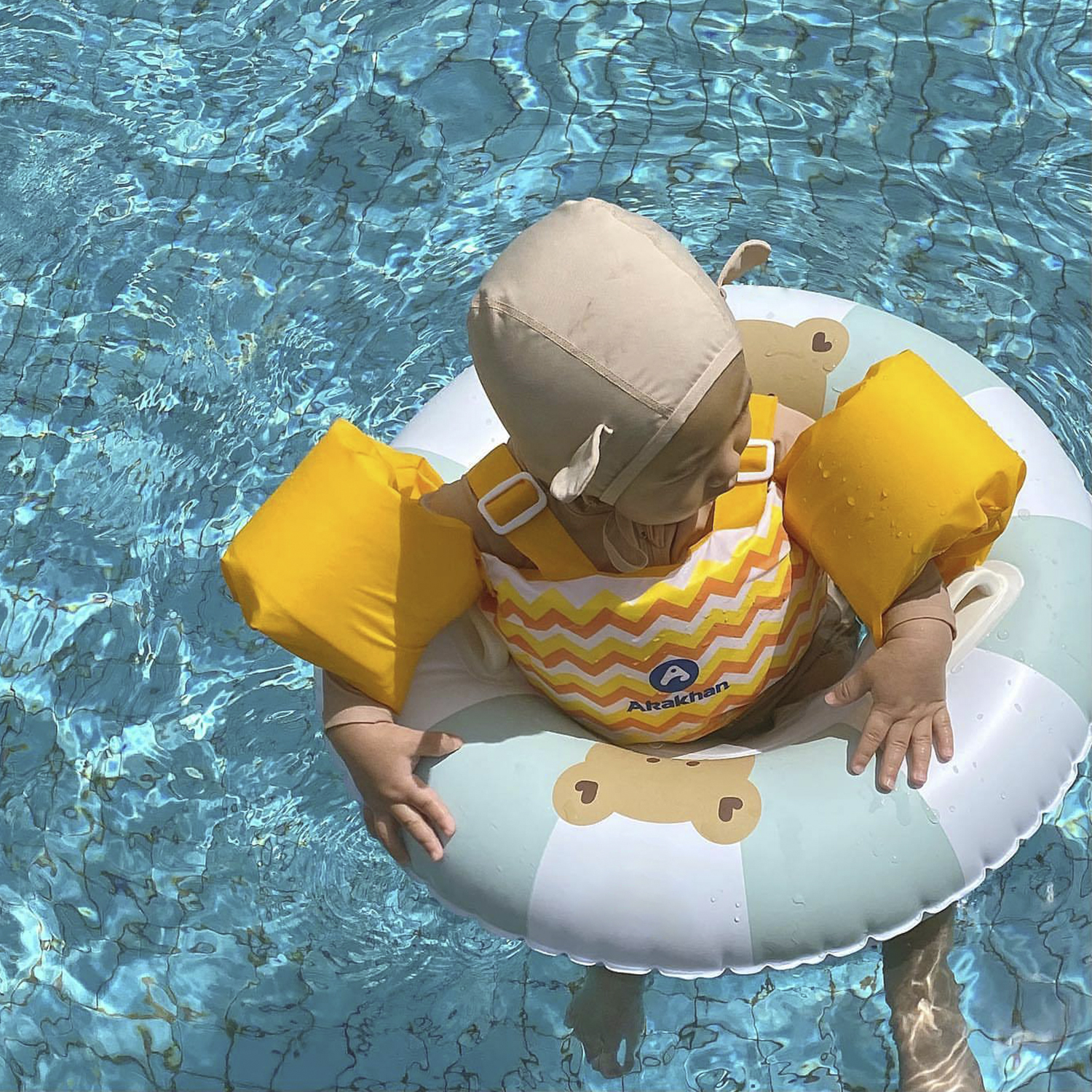 Un bebé con traje de baño y flotador en una piscina, usando gorro de natación.