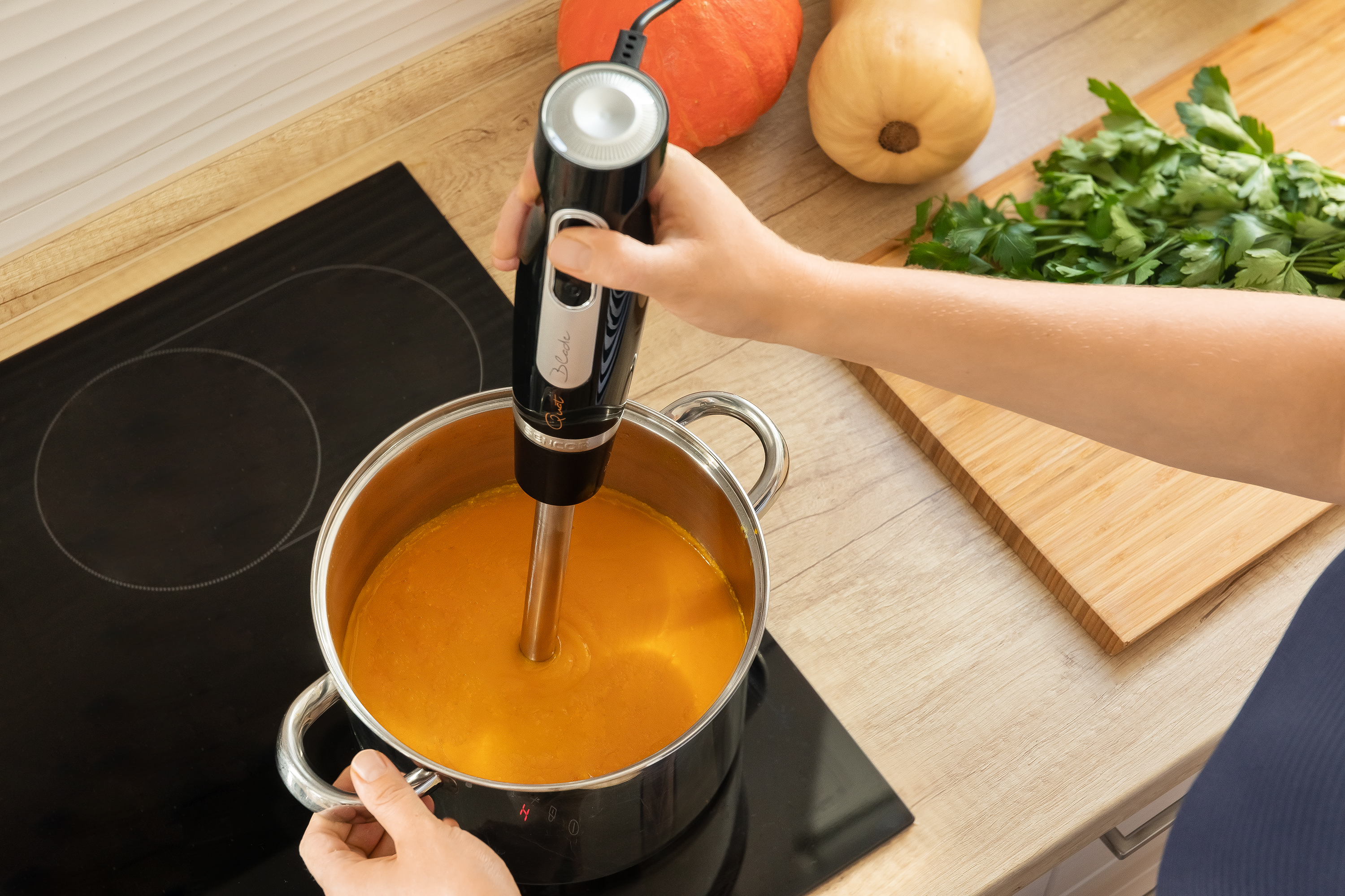 Osoba miksuje zupę w garnku za pomocą blendera ręcznego.