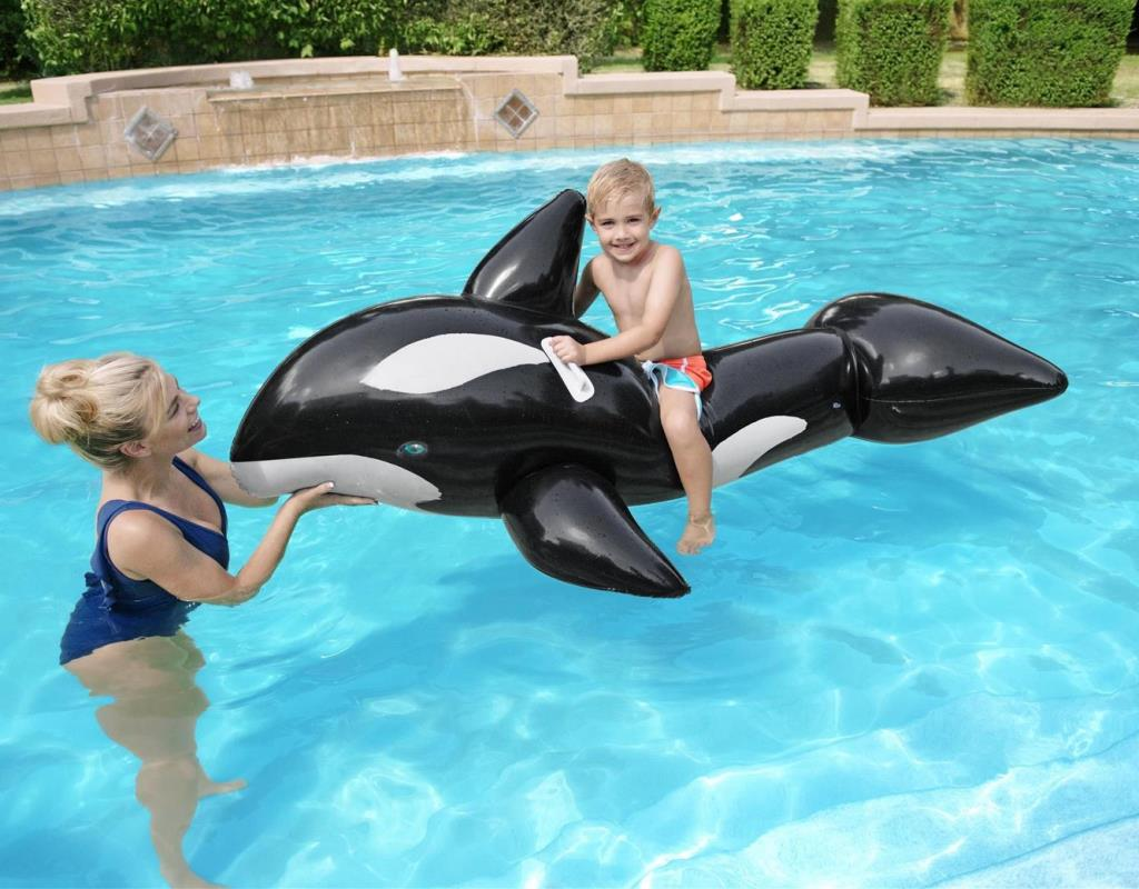 Una mujer y un niño en un flotador de orca blanco y negro en una piscina.