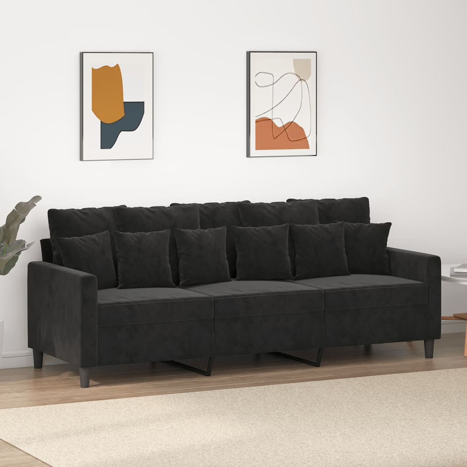 Ein schwarzes Samtsofa mit sechs Kissen vor einer weißen Wand mit Kunstdrucken.