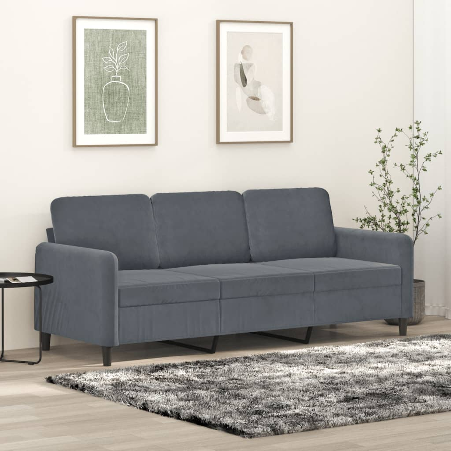 Ein graues Dreisitzer-Sofa vor einer weißen Wand mit zwei gerahmten Bildern und einem Teppich.