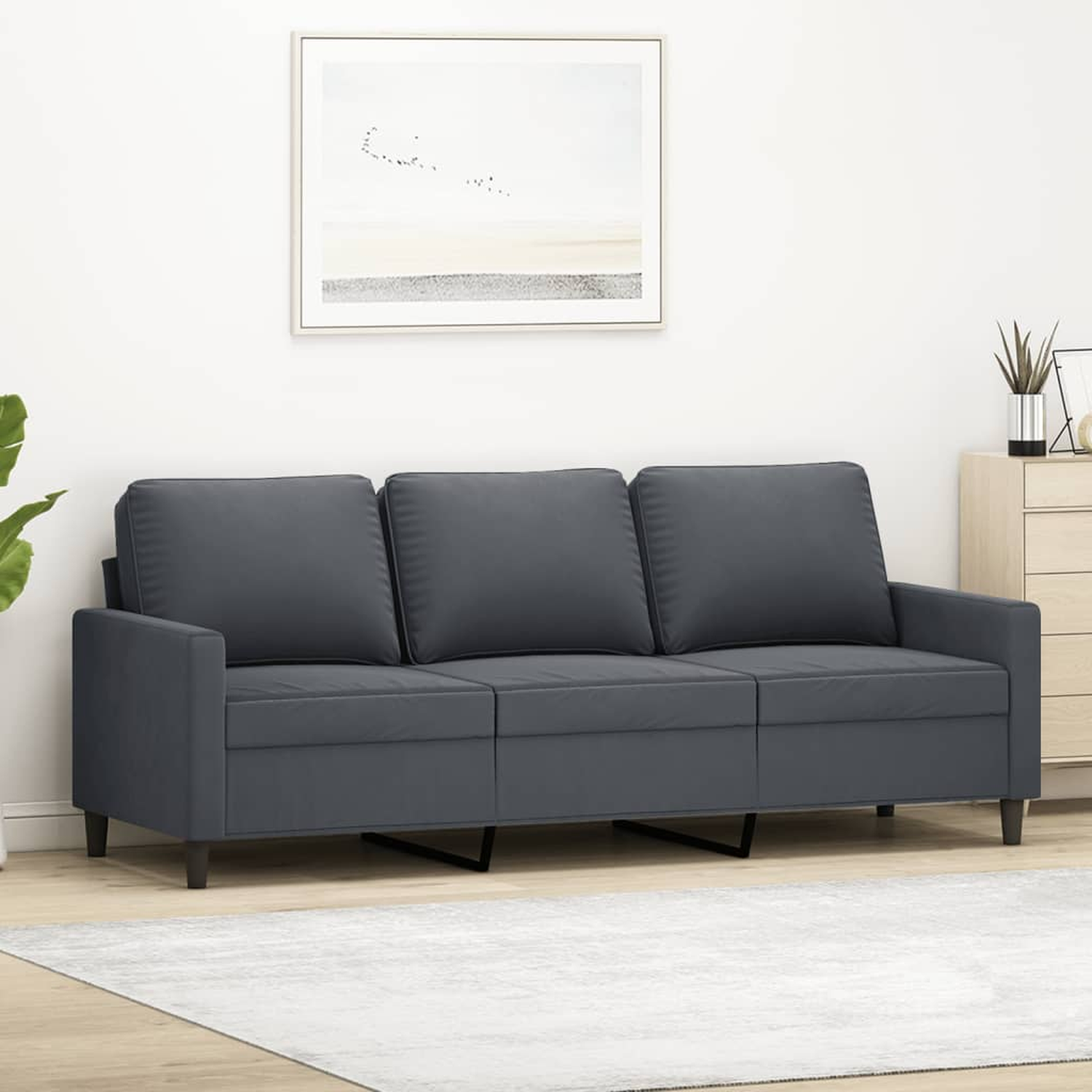 Graues Stoffsofa mit drei Kissen auf einem weißen Teppich, mit Bild und Möbeln im Hintergrund.