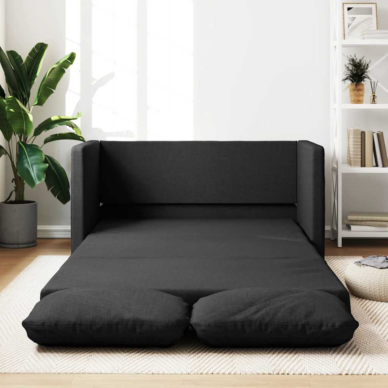 Ein dunkelgraues Schlafsofa, ausgeklappt, mit zwei Kissen auf einem Teppich.