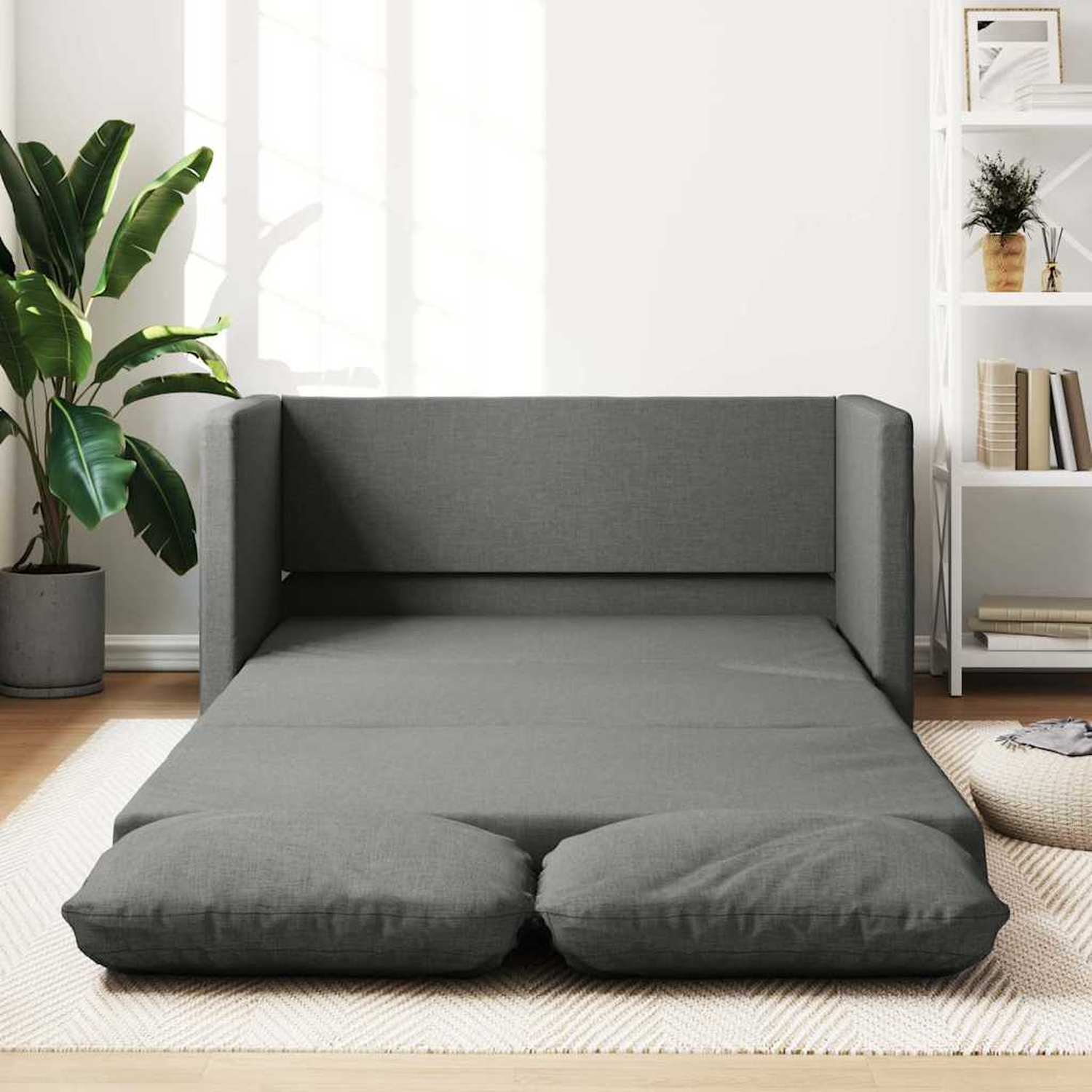 Ein graues Schlafsofa geöffnet. Zwei Kissen liegen auf dem Boden.