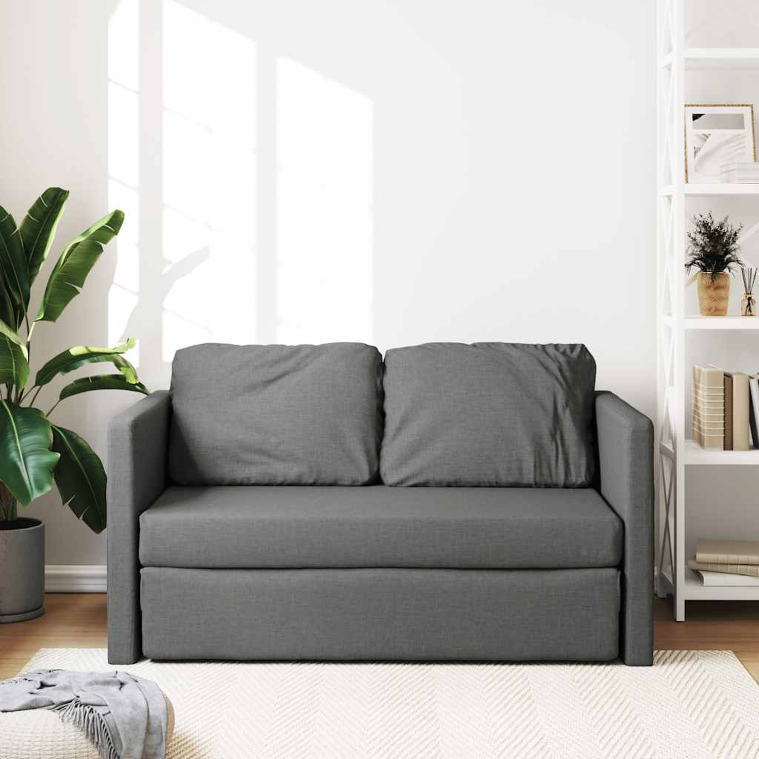 Graues Sofa mit zwei Kissen, einer Pflanze und einem Bücherregal.