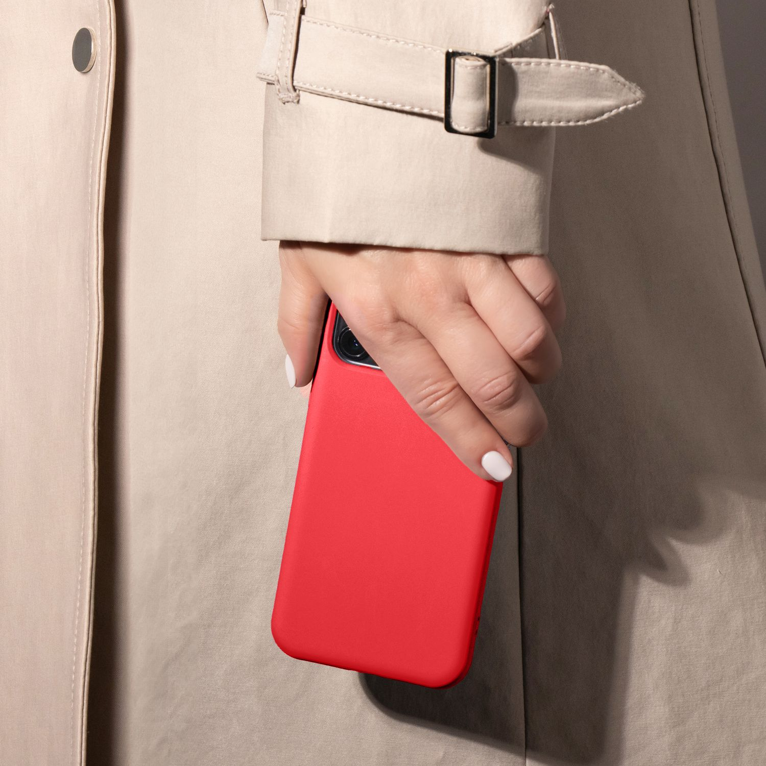 Eine Hand hält eine rote Handyhülle. Die Person trägt einen beigen Trenchcoat.