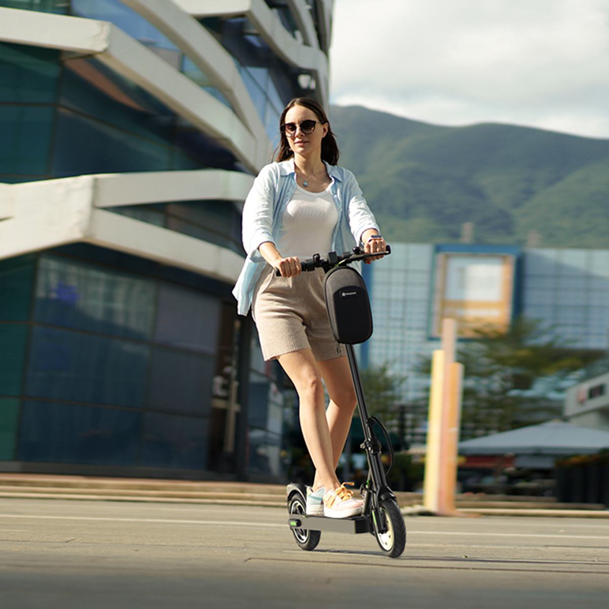 Kobieta jedzie na hulajnodze elektrycznej po utwardzonej drodze w mieście, słoneczny dzień.