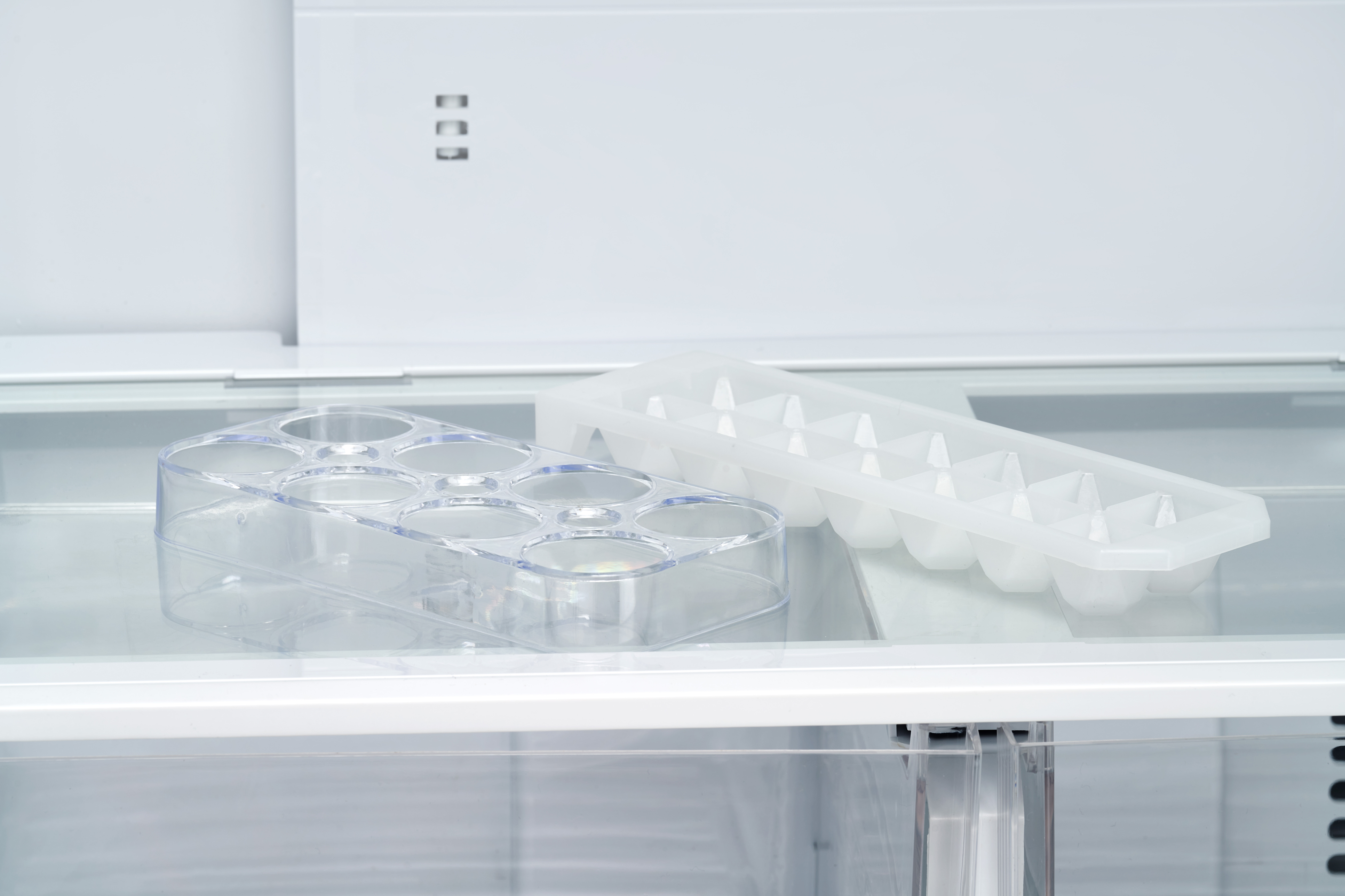 In einem Kühlschrank zwei durchsichtige Eiswürfelschalen. Eine hat sechs runde Formen, die andere viele kleine Dreiecke.