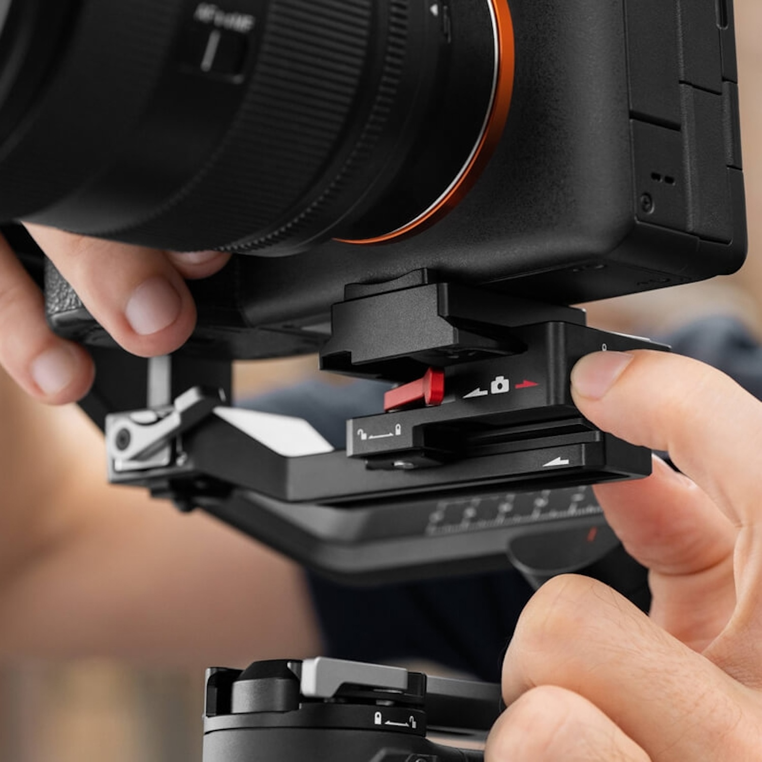 Hände halten eine Kamera, die an einem Gimbal-Stabilisator befestigt ist. Roter Verriegelungsknopf sichtbar.