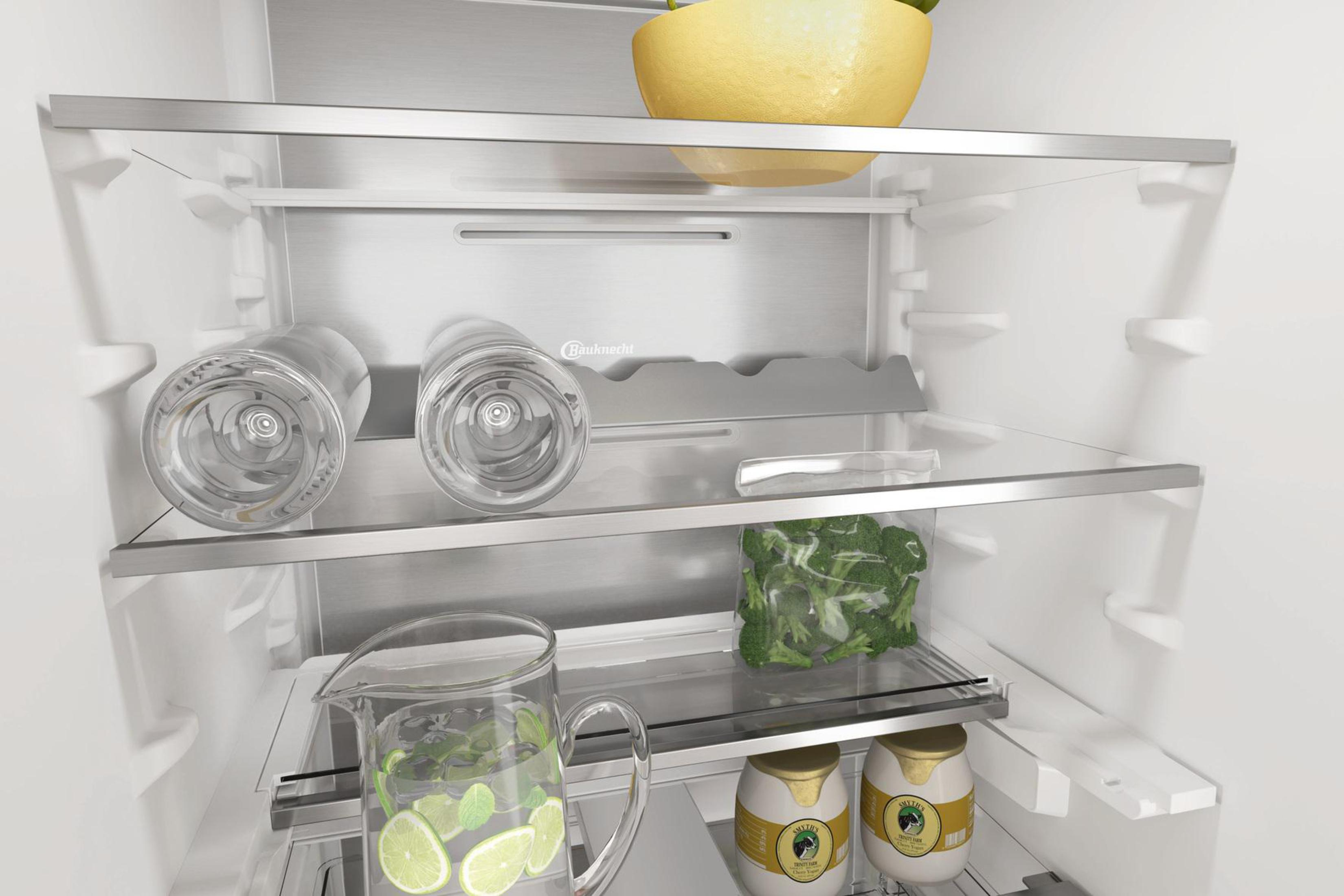 Kühlschrankinnenraum. Glasregale, Flaschen, Gläser und eine Schüssel mit gelbem Obst.