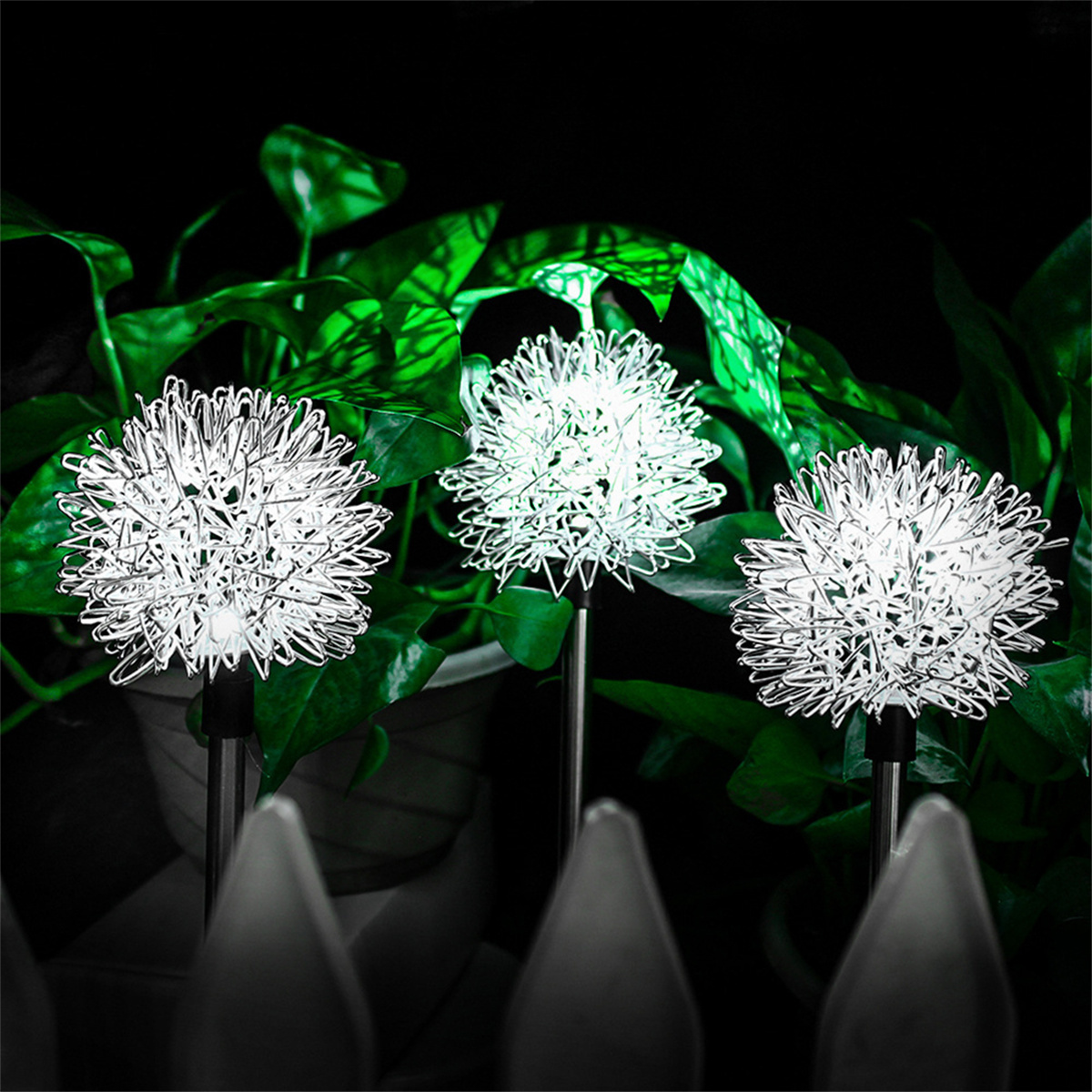 Drei beleuchtete dekorative Lichter in einem Garten, mit grünem Laub im Hintergrund.