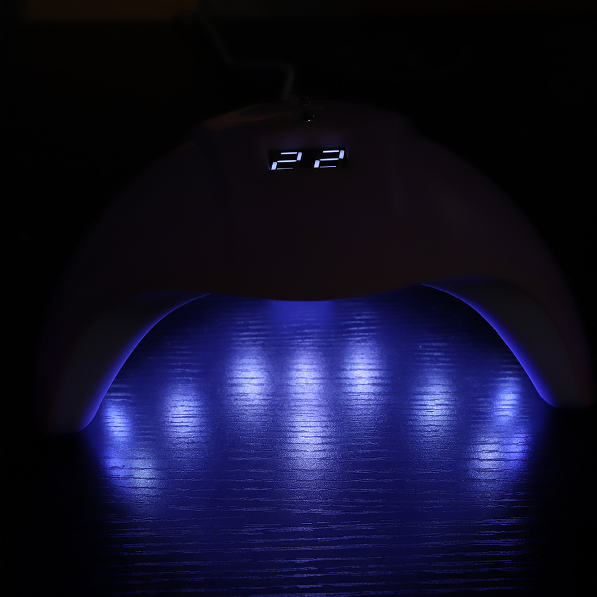 UV-Nagellampe mit blauem Licht, das auf eine Holzoberfläche scheint.