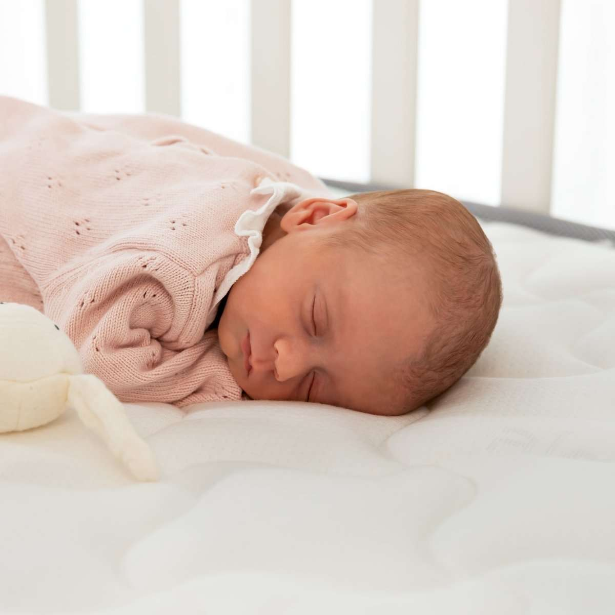 Bebé recién nacido durmiendo en cuna. Manta de punto rosa. Ropa de cama blanca, cuna blanca, fondo borroso.