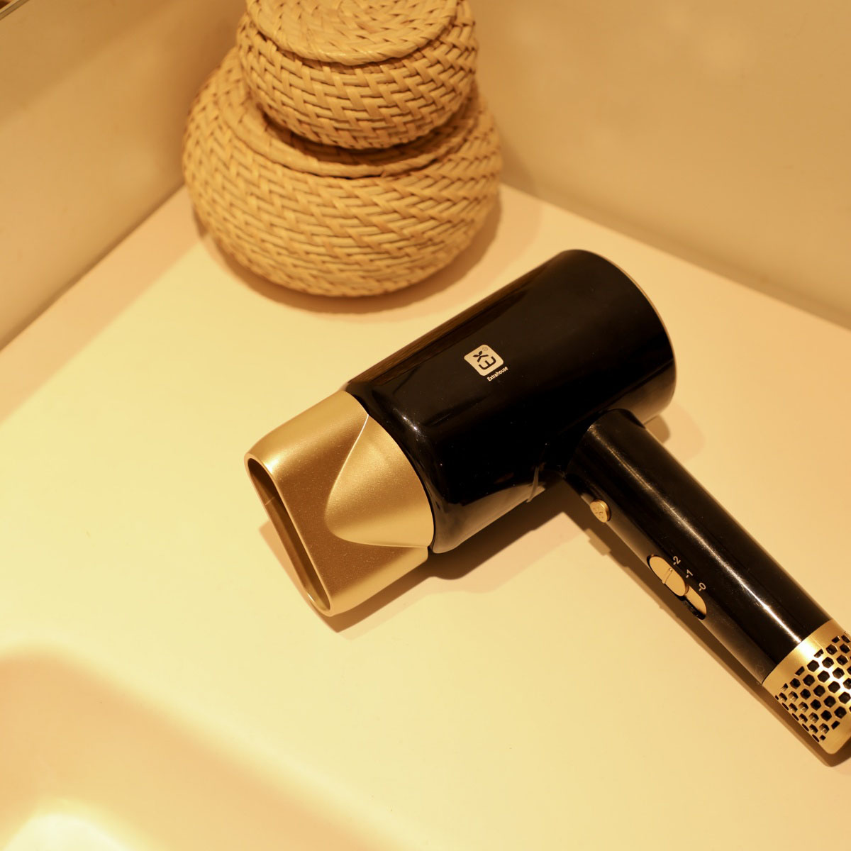 Un secador de pelo negro y dorado sobre una superficie beige con dos cestas tejidas.