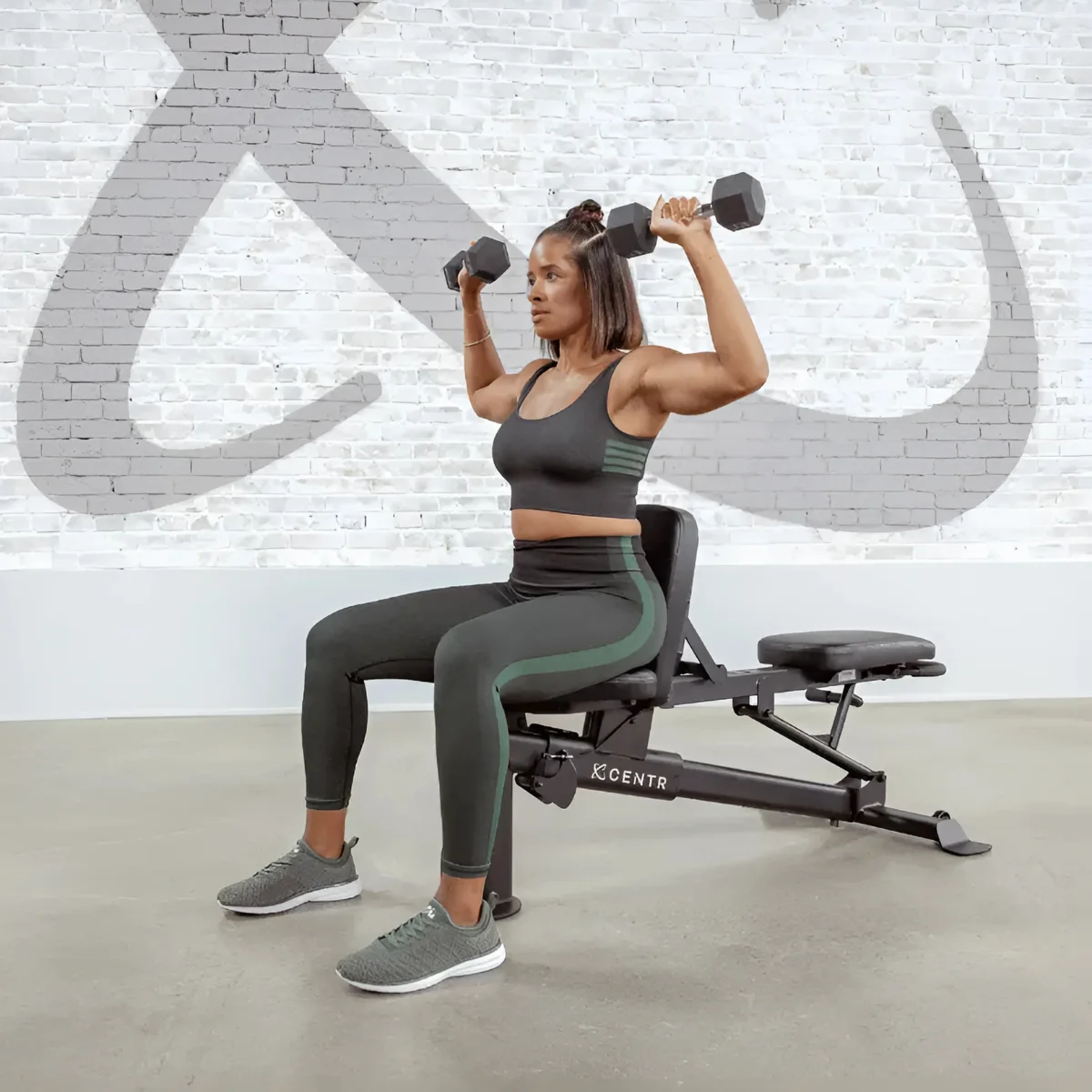 Woman exercising, lifting dumbbells while sitting on a workout bench.