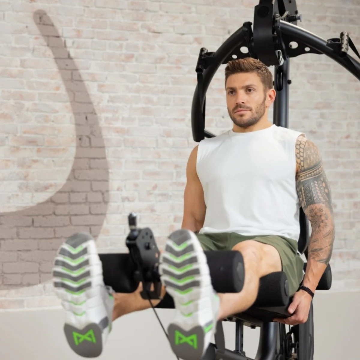 Ein Mann trainiert seine Beine an einer Fitnessmaschine, Ziegelwand im Hintergrund.