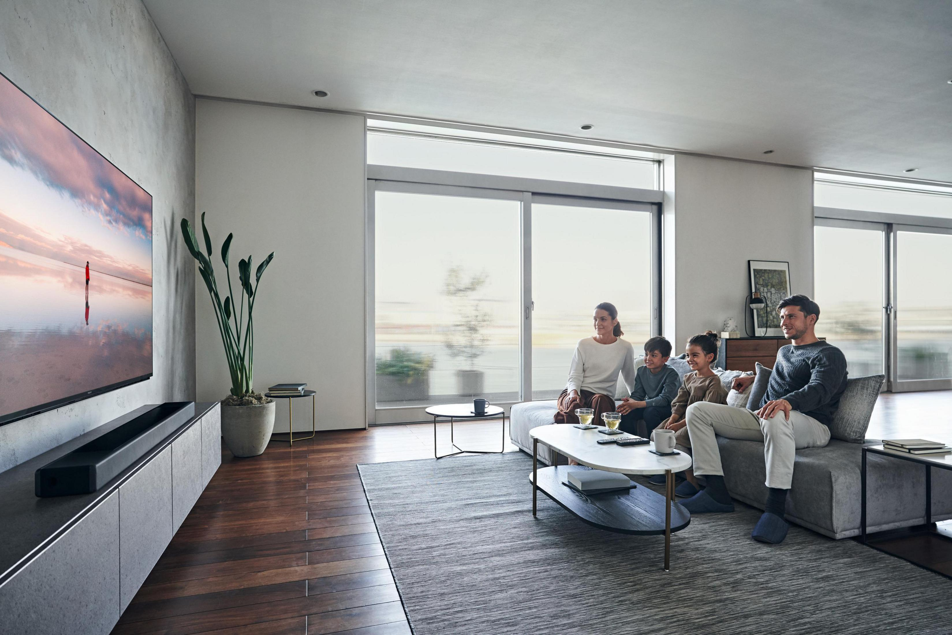 Eine Familie schaut im modernen Wohnzimmer fern. Der Fernseher zeigt eine farbenfrohe Landschaft.