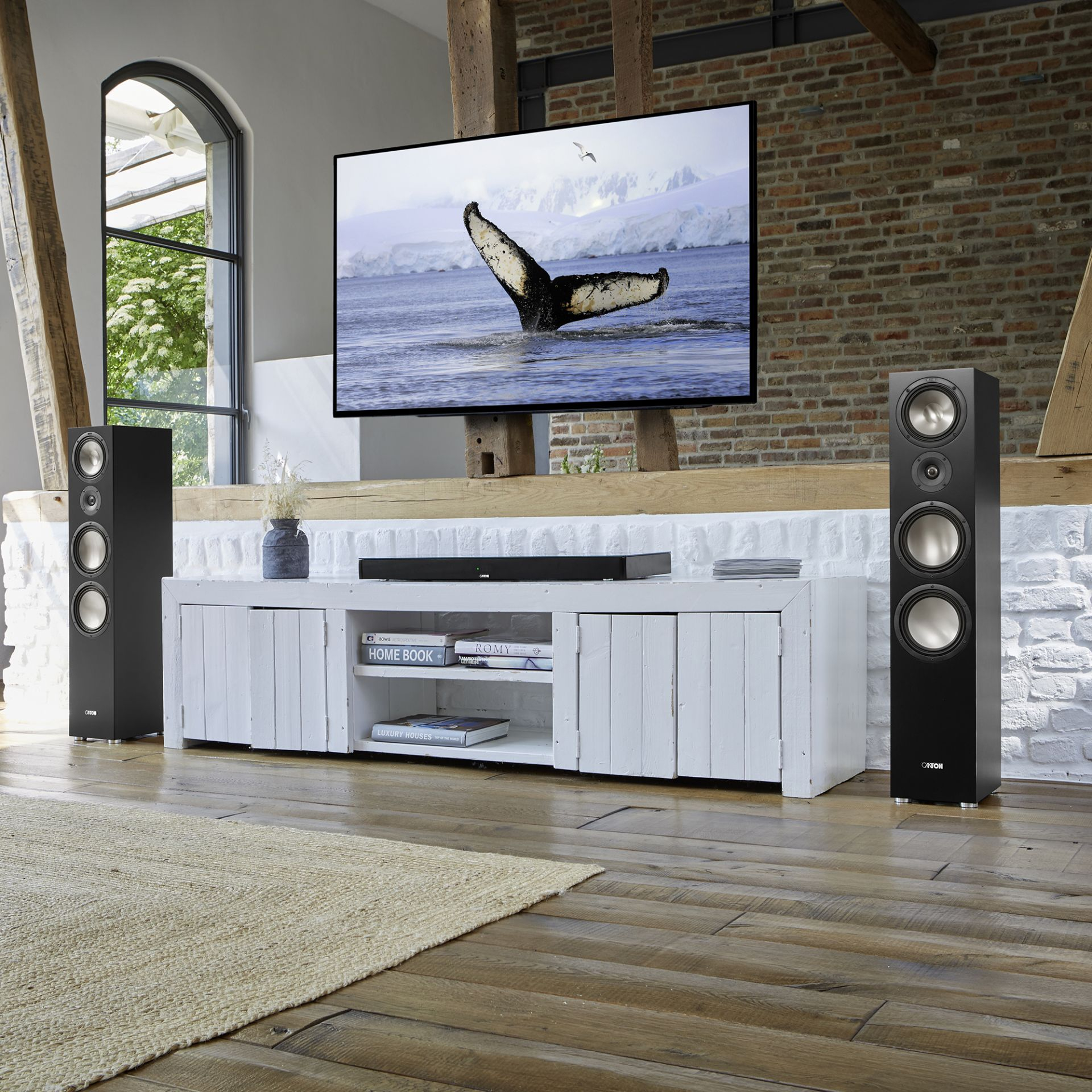 Wohnzimmer mit großem Fernseher, Lautsprechern und einem weißen Schrank.