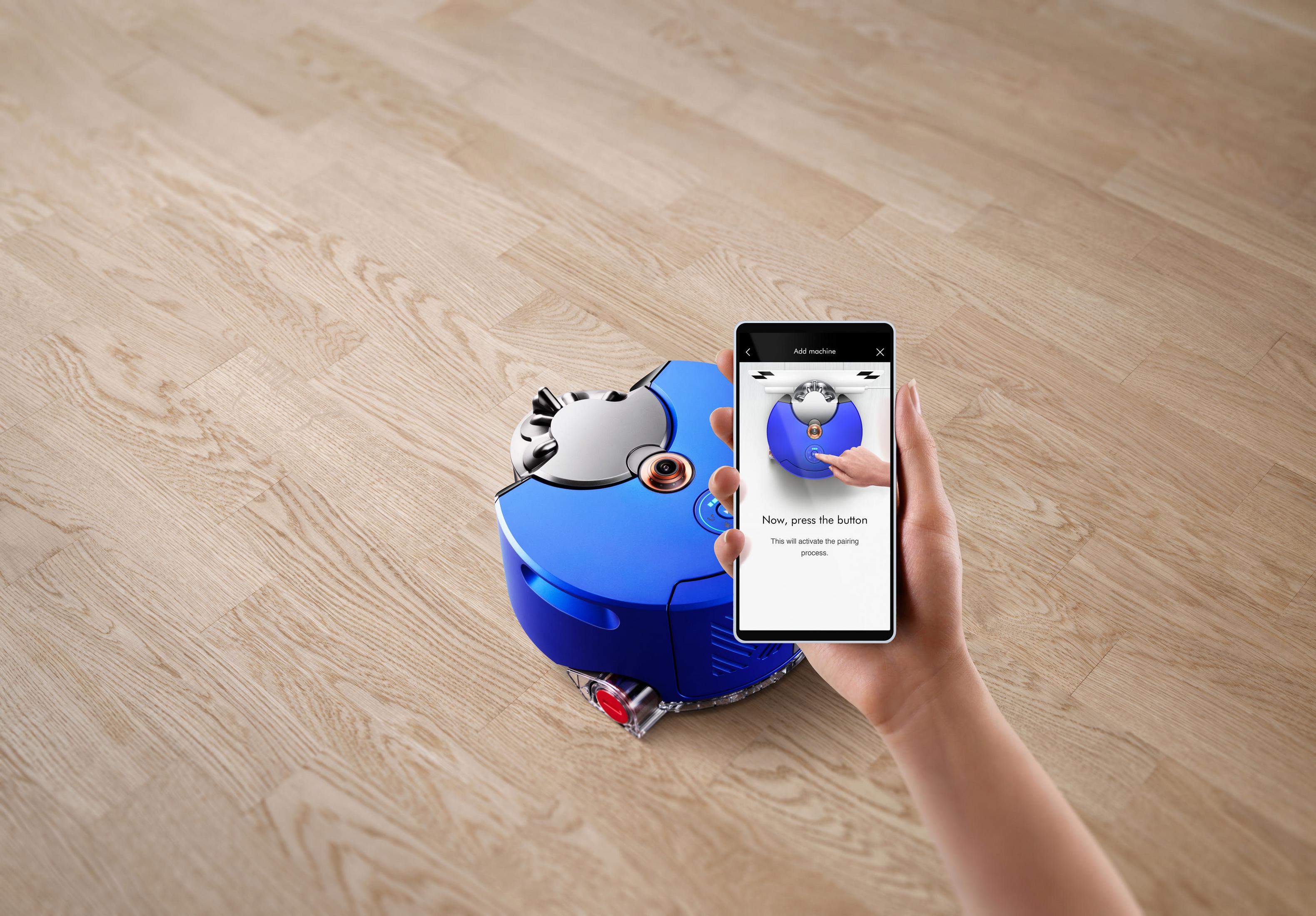 Blauer Roboterstaubsauger und Telefon mit Kopplungsanzeige auf Holzfußboden.