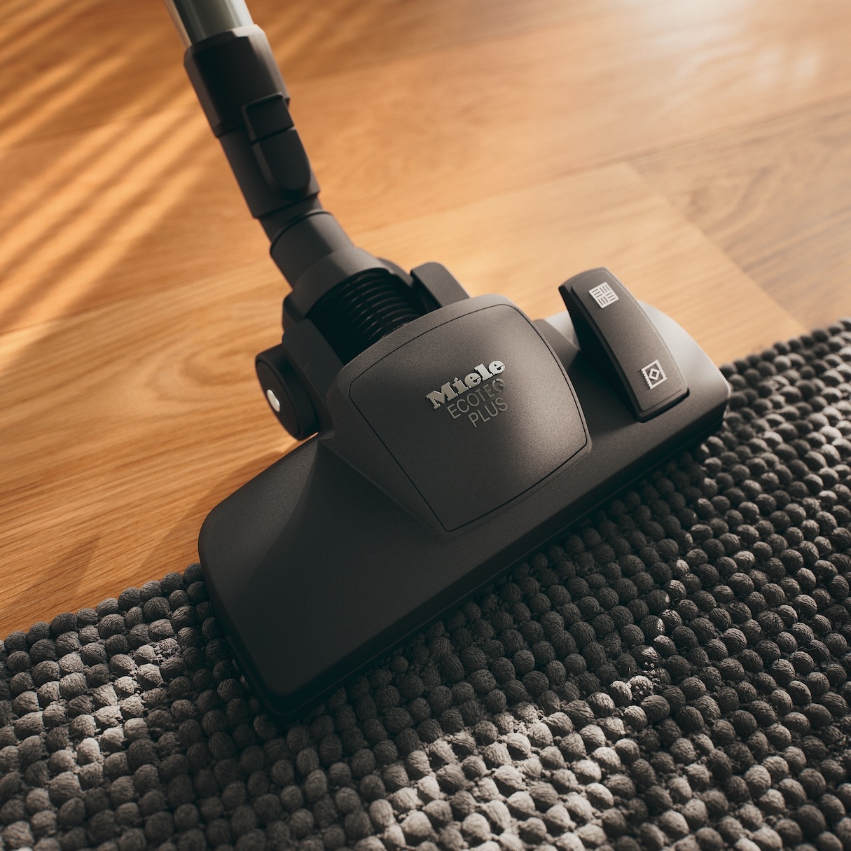 Staubsaugerkopf auf grauem Teppich und Holzboden. Miele Ecoline Plus.