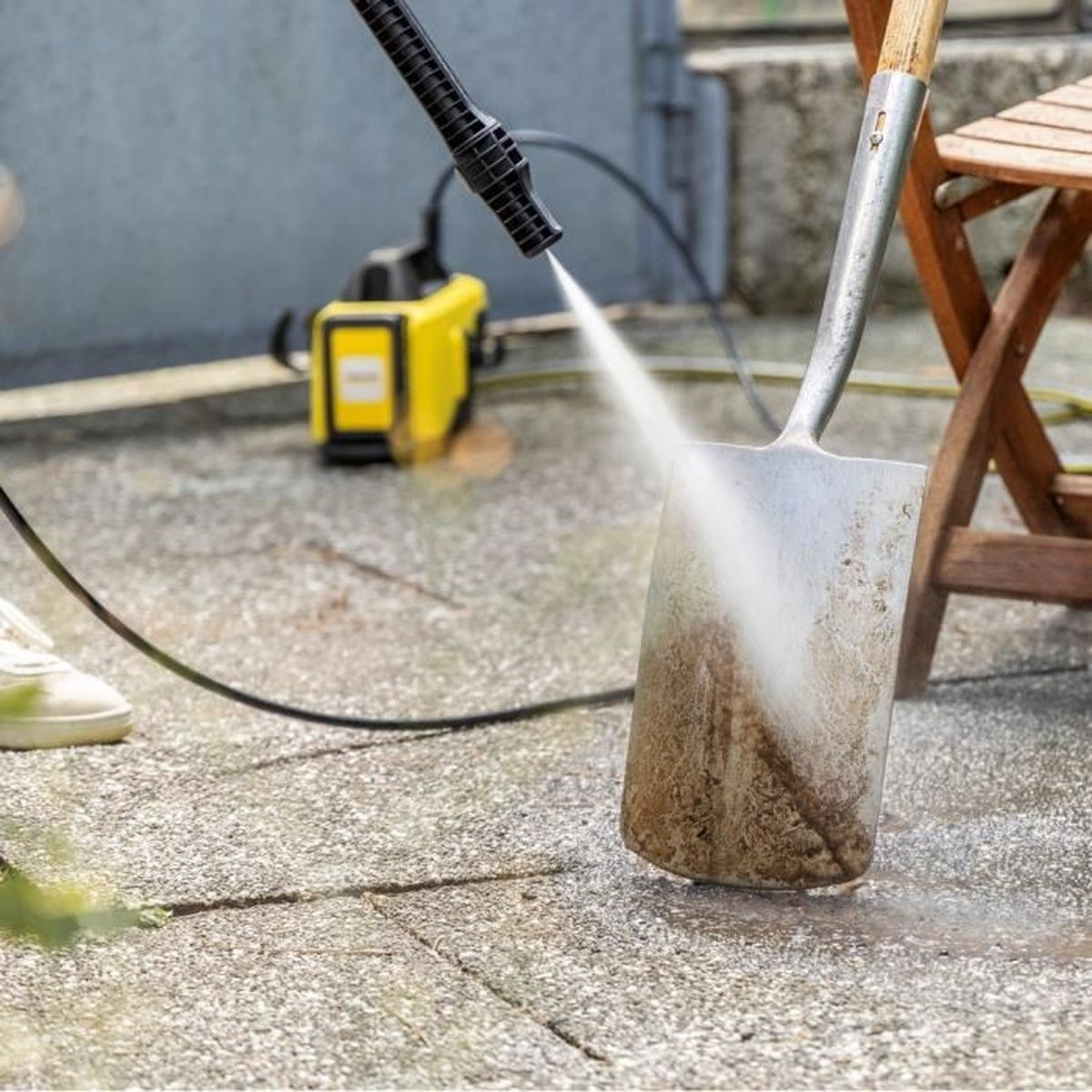 Un'idropulitrice spruzza acqua su una pala su una superficie di cemento, creando una pulizia.