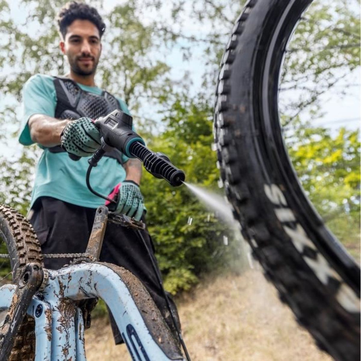 Un uomo che pulisce una mountain bike fangosa con un'idropulitrice, all'aperto.