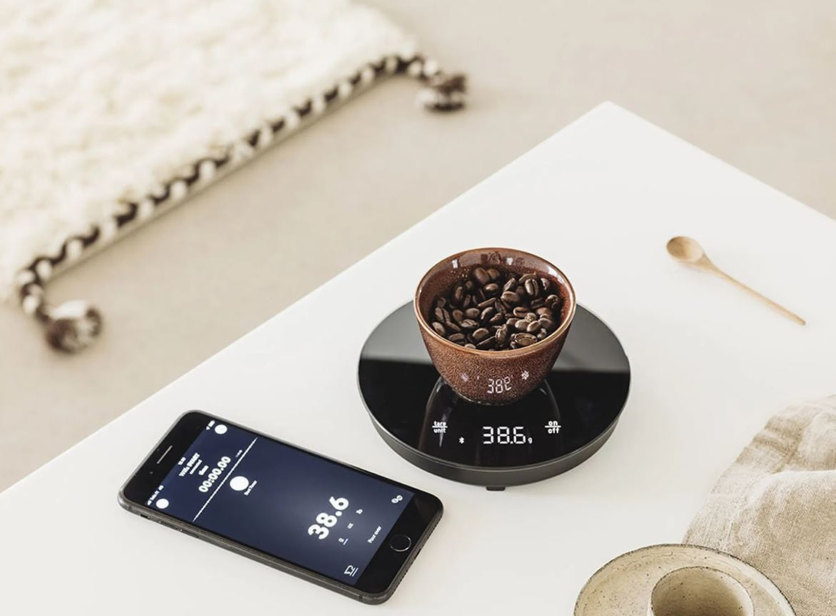 Kaffeebohnen in einer Schale auf einer Waage mit einem Telefon, das einen Timer und Gewicht anzeigt.