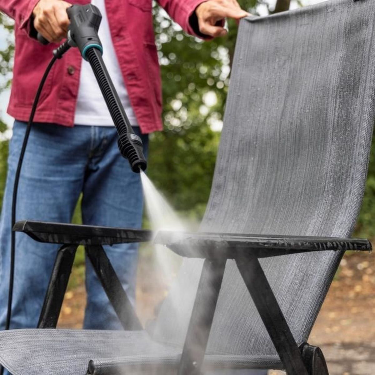 Une personne utilise un nettoyeur haute pression pour nettoyer une chaise grise extérieure.